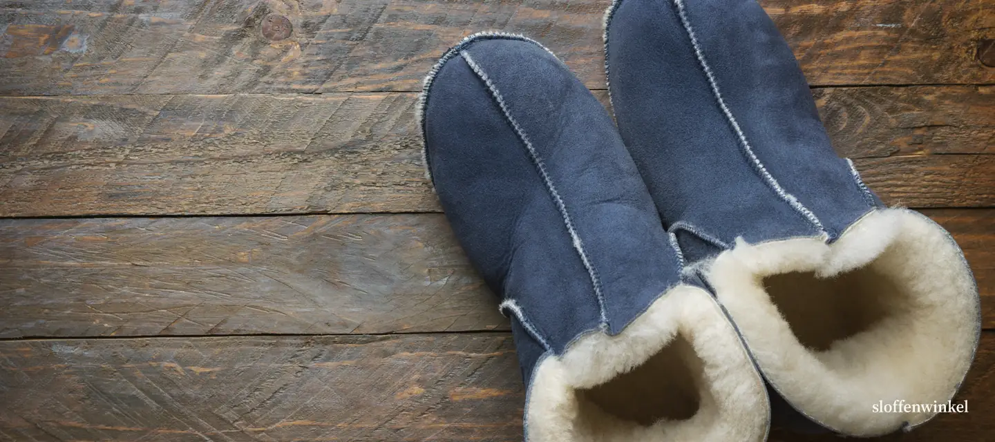 Blauwe suède sloffen met schapenvacht op een donkere houten vloer